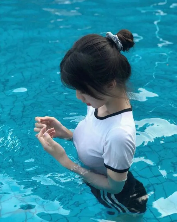 Cô gái trong nước xanh, tóc búi gọn, quay nghiêng mặt, da sáng nổi bật và khỏe khoắn.