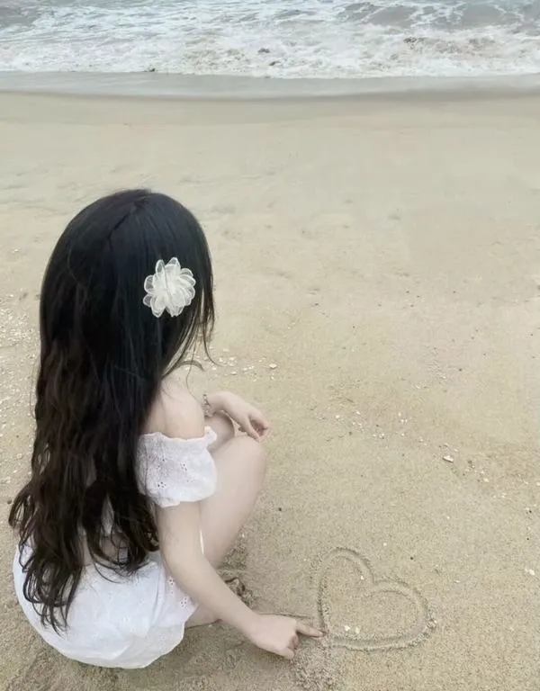 Cô gái ngồi trên cát trắng, kẹp hoa trên tóc, lưng quay camera, vẻ dịu dàng rất lâu.