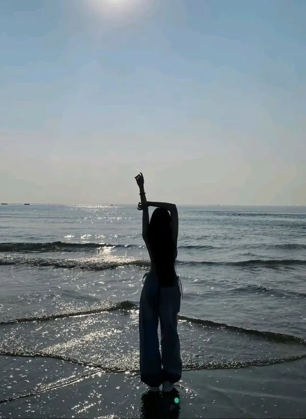 Ảnh gái đi biển không lộ mặt, cô gái giơ tay tạo dáng, nền biển yên, mood tối giản.